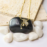 A gold necklace with a textured leaf pendant resting on a polished black stone, styled with white and beige stones on a white surface.