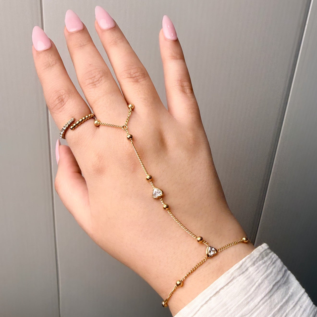 Hand wearing multiple gold bracelets on a neutral background