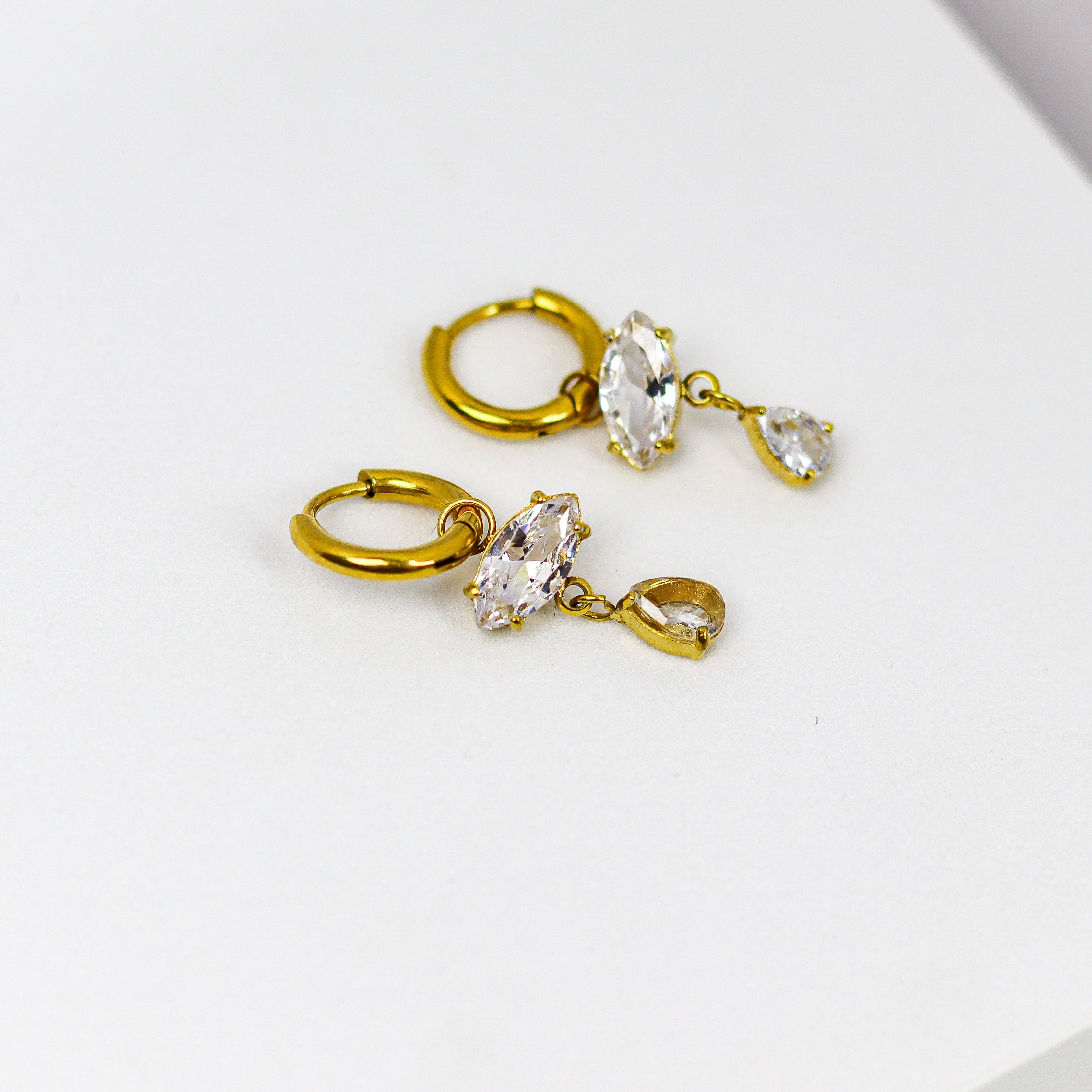 These earrings exude elegance with their dangling marquise and teardrop-shaped stones set in a golden frame