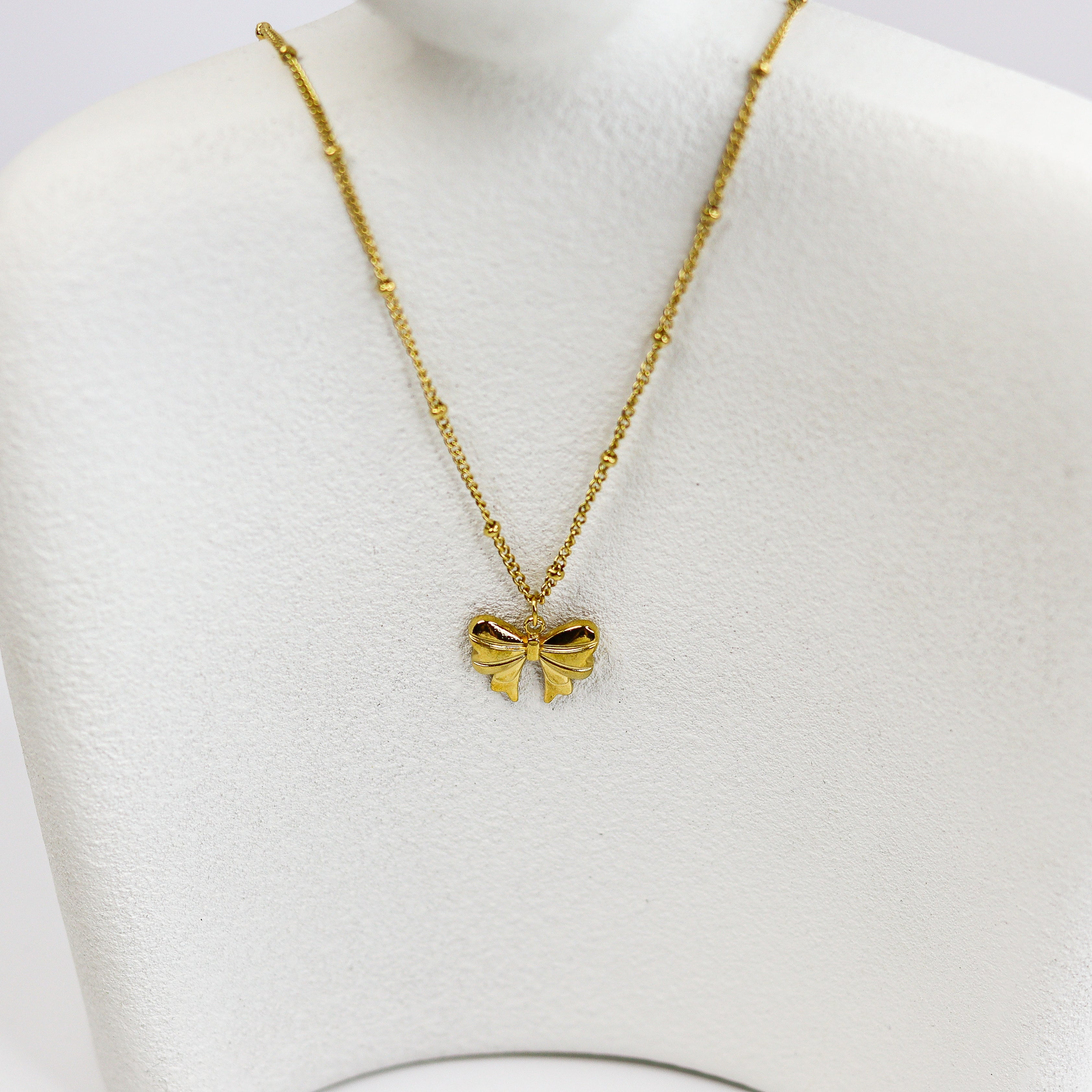Gold bow-shaped necklace on a mannequin bust against a white background