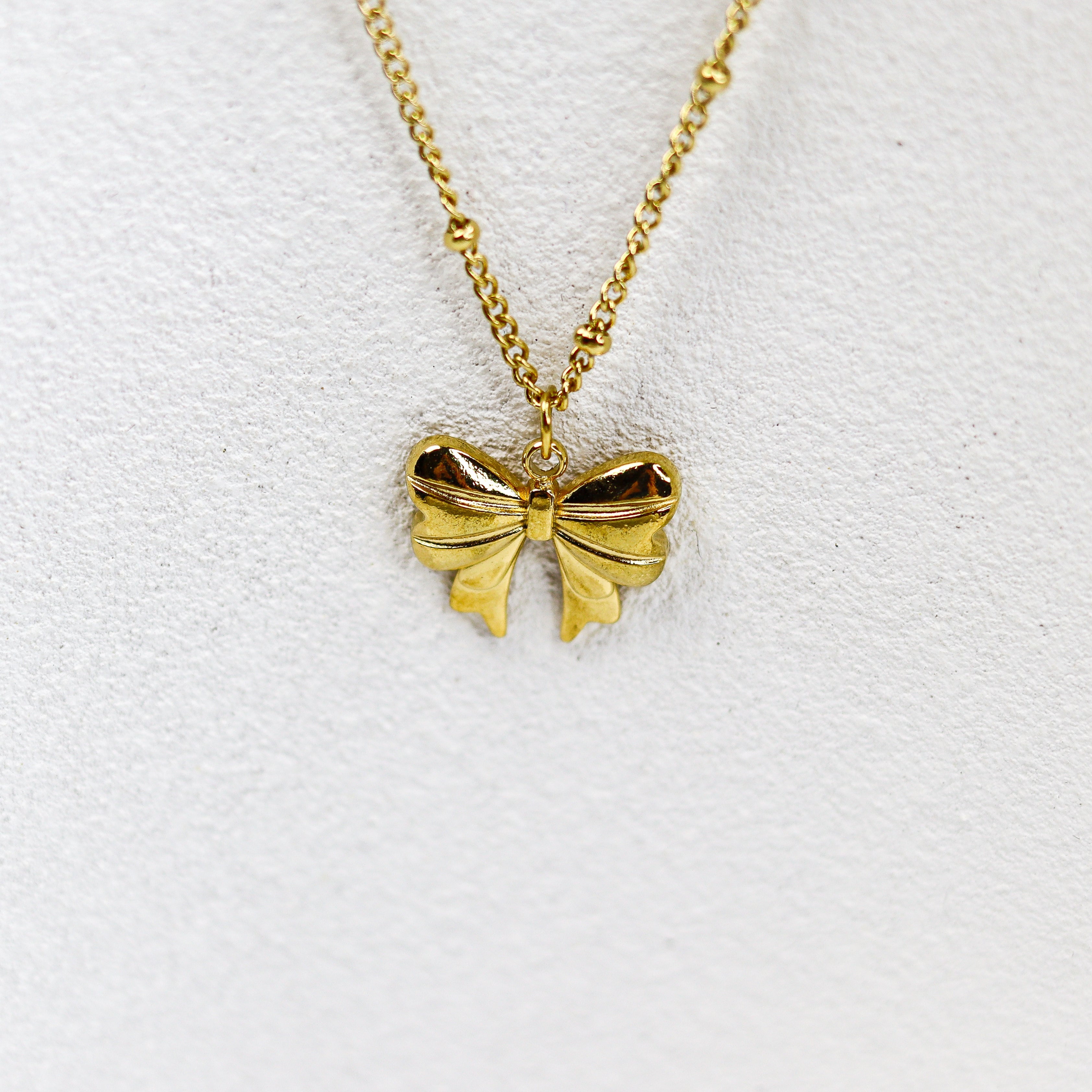 Gold bow-shaped pendant on a gold chain against a white background
