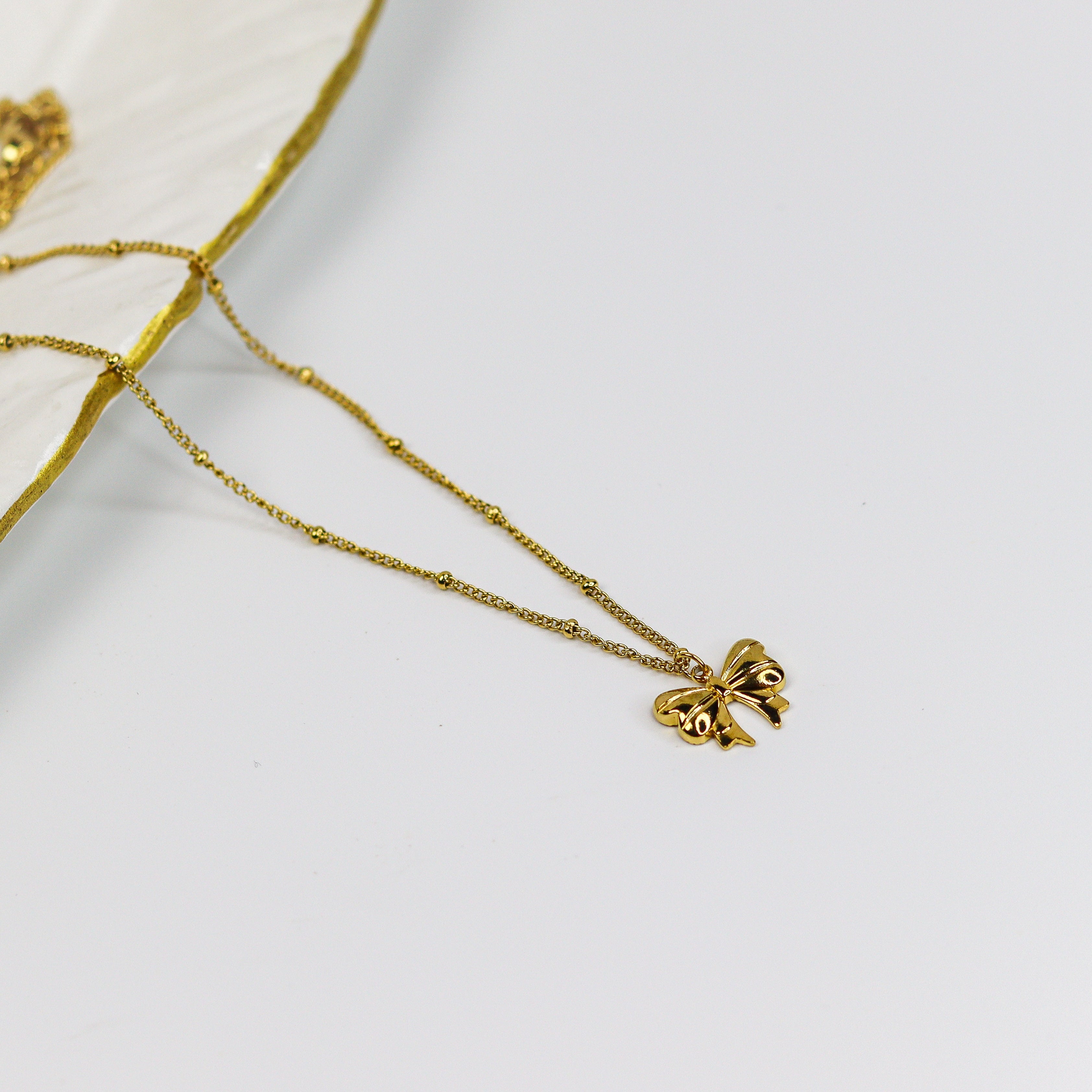 Gold necklace with a Ribbon bow pendant on a white background