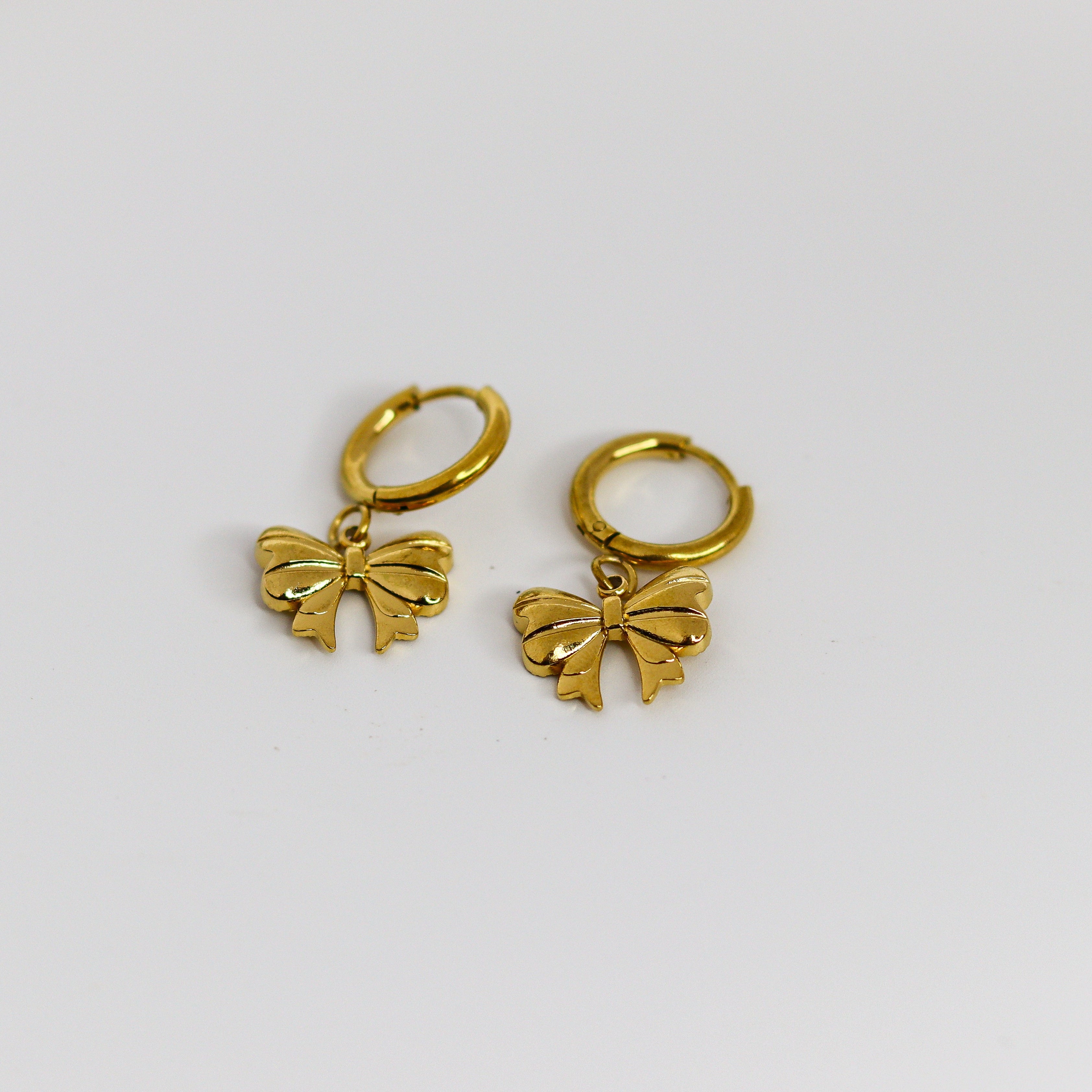Two gold bow-shaped charms hoops on a white background