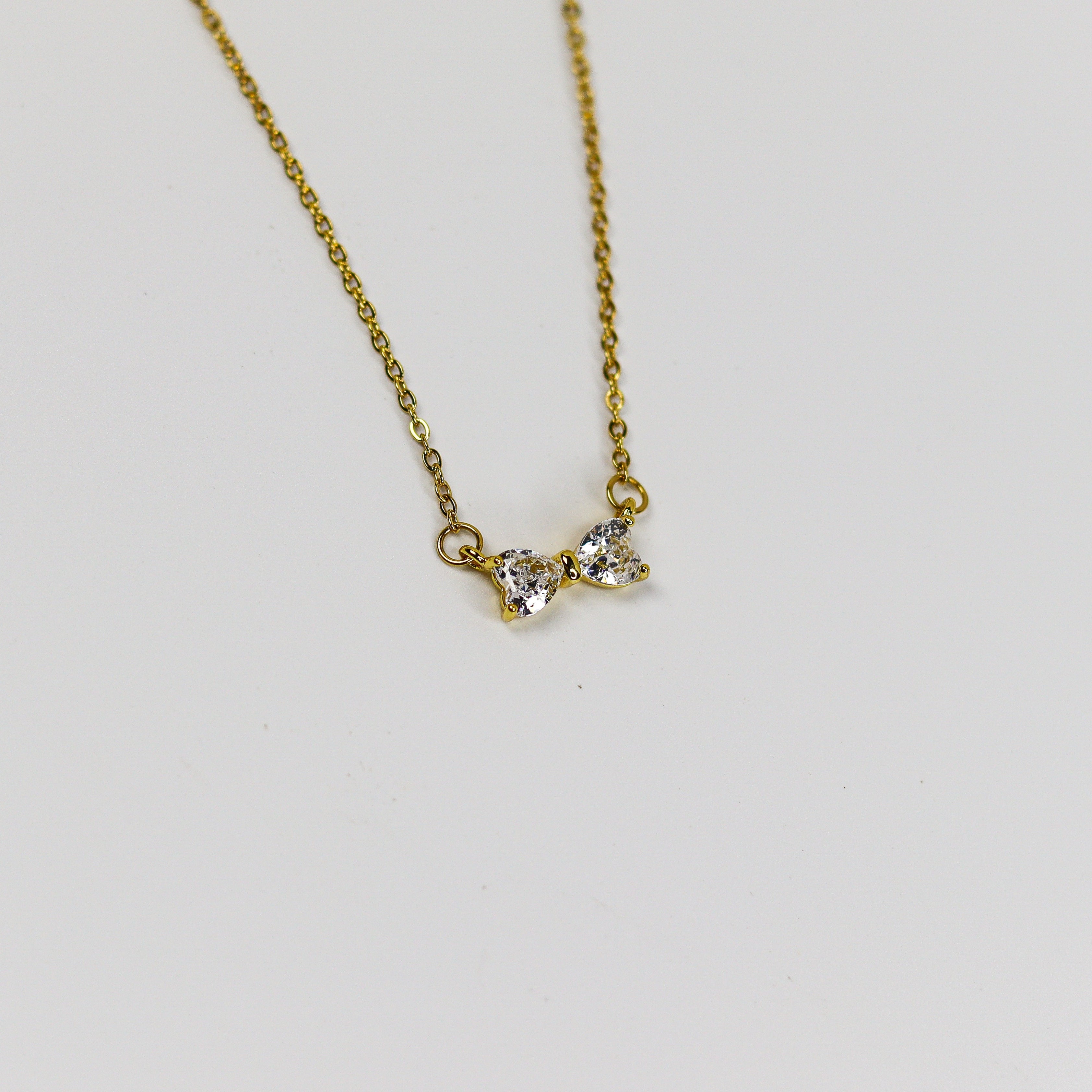 Minimalist bow necklace featuring twin heart-cut stones set in a polished gold frame on a fine link chain.