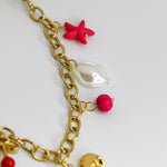 Chunky gold-tone chain necklace with statement bow and colorful enamel charms — cherries, starfish, beads, and a pearl drop.