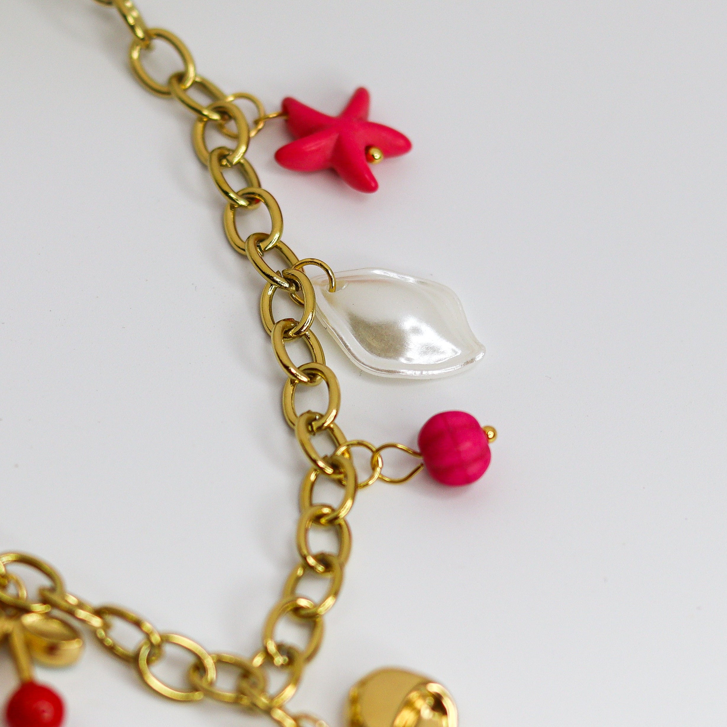 Chunky gold-tone chain necklace with statement bow and colorful enamel charms — cherries, starfish, beads, and a pearl drop.