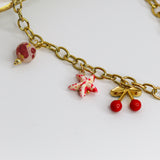 Chunky gold-tone chain necklace with statement bow and colorful enamel charms — cherries, starfish, beads, and a pearl drop.
