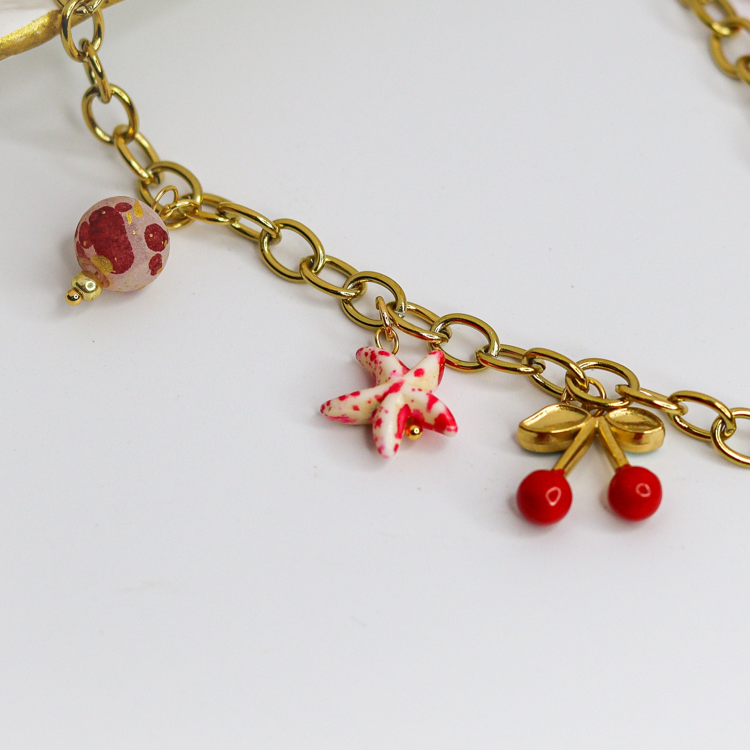 Chunky gold-tone chain necklace with statement bow and colorful enamel charms — cherries, starfish, beads, and a pearl drop.