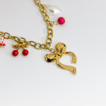 Chunky gold-tone chain necklace with statement bow and colorful enamel charms — cherries, starfish, beads, and a pearl drop.