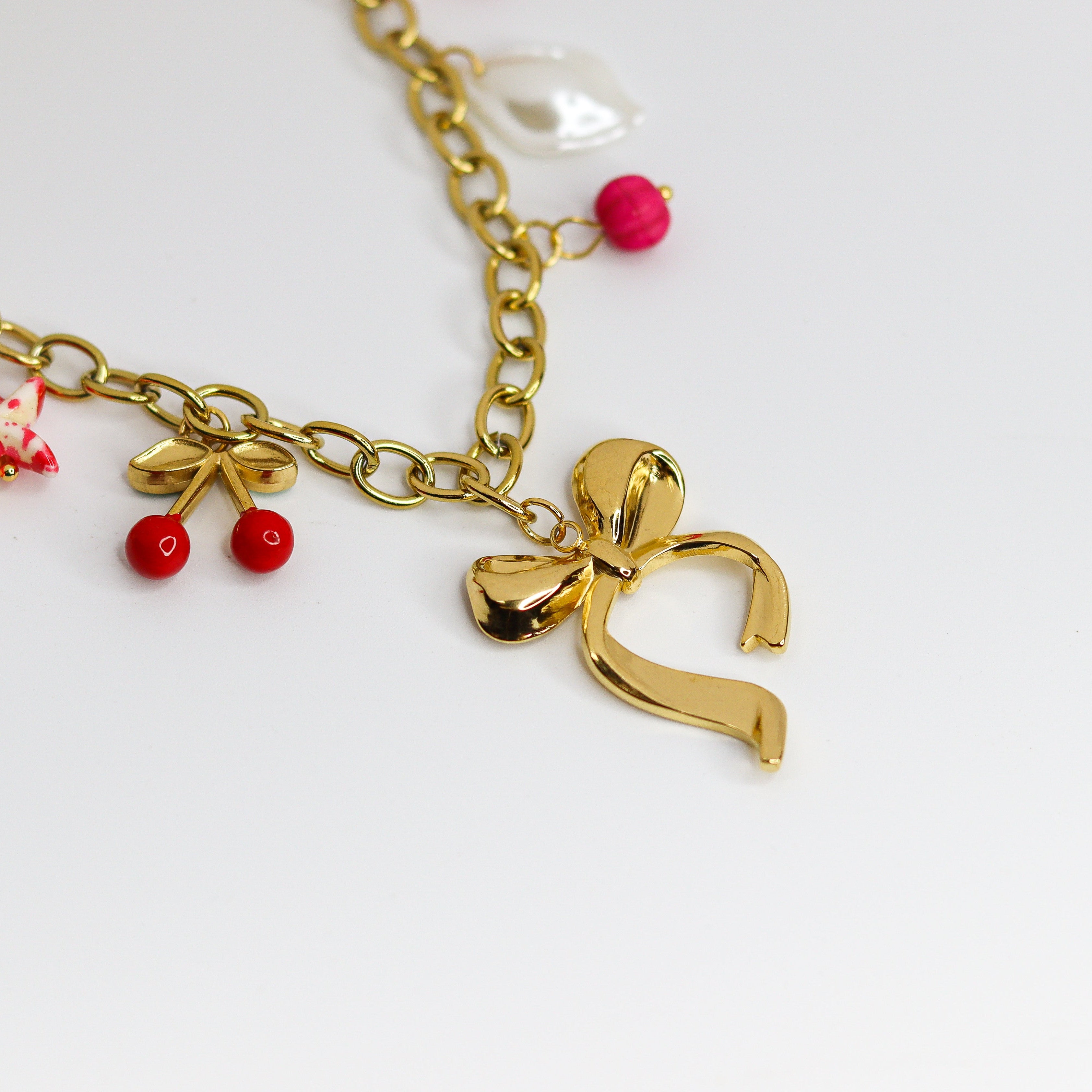 Chunky gold-tone chain necklace with statement bow and colorful enamel charms — cherries, starfish, beads, and a pearl drop.