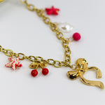 Chunky gold-tone chain necklace with statement bow and colorful enamel charms — cherries, starfish, beads, and a pearl drop.