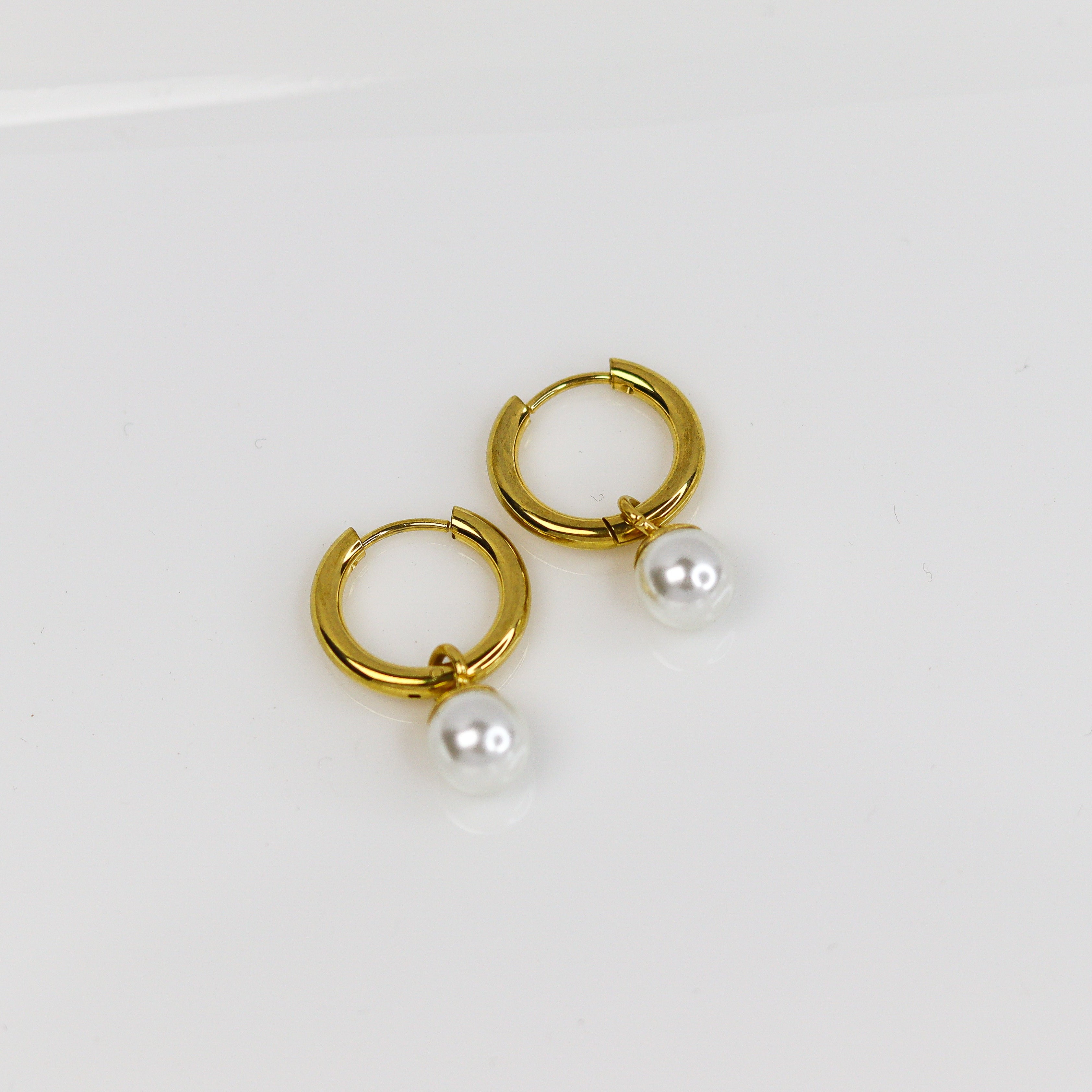 Gold hoop earrings with pearl drops on a white background