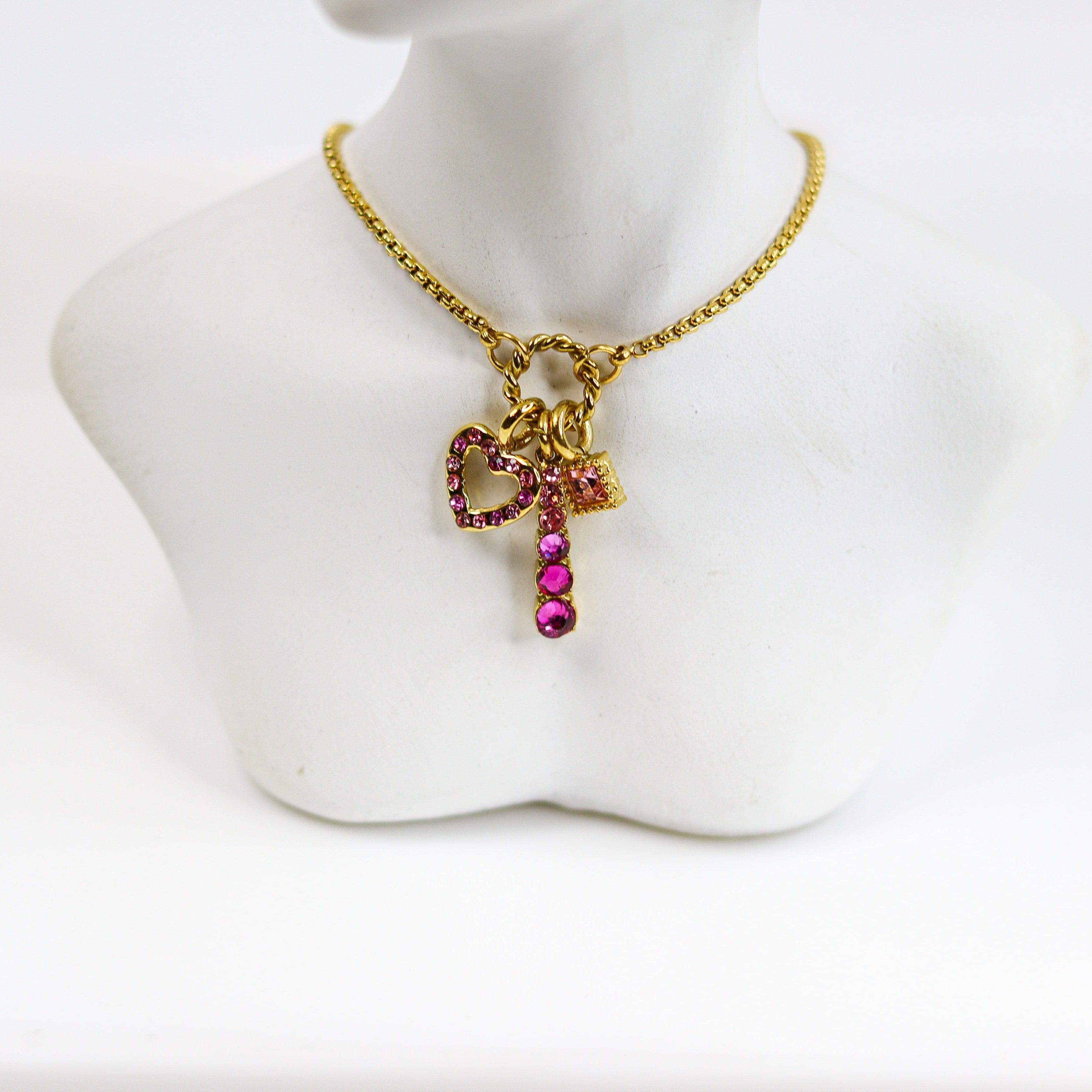 Gold necklace with a bow-shaped pendant and pink gemstones on a mannequin bust.