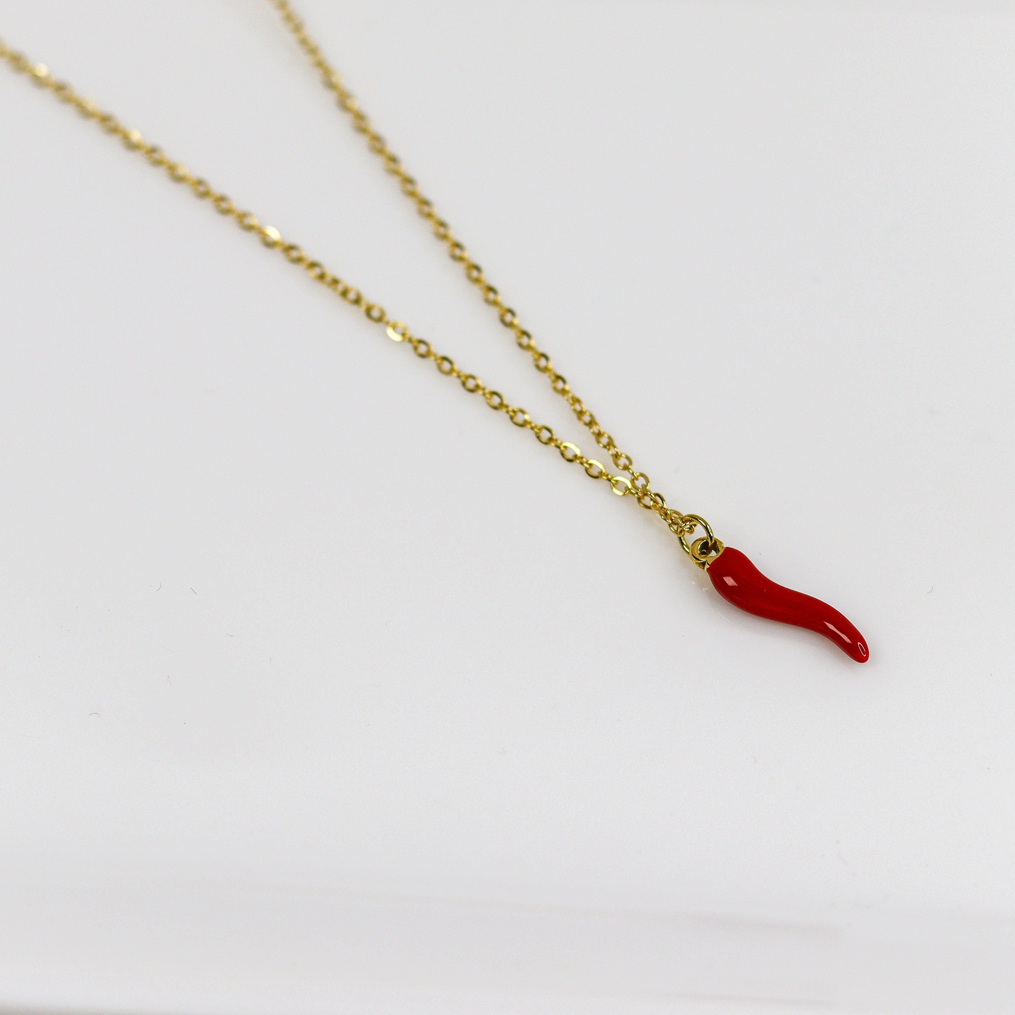 Gold necklace with a red chili pepper pendant on a white background