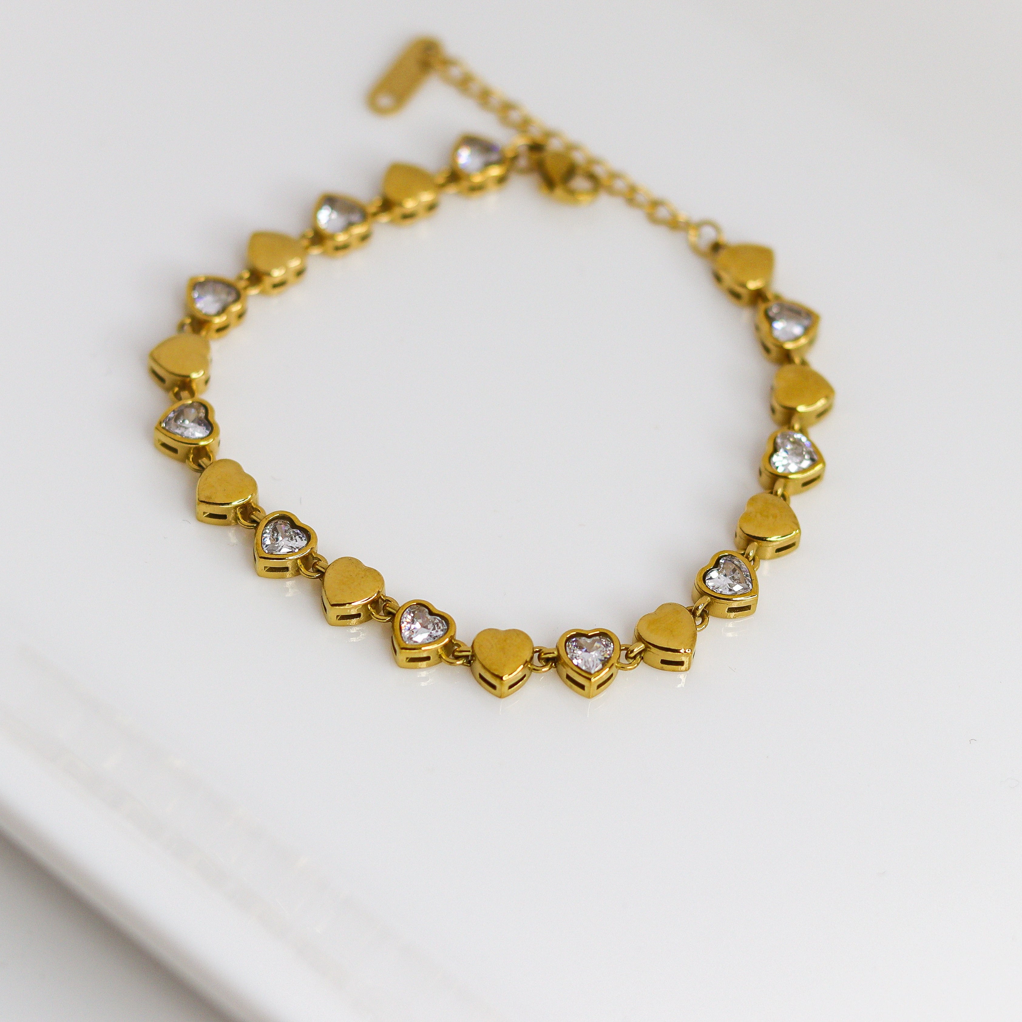 Gold bracelet with heart-shaped links on a white surface