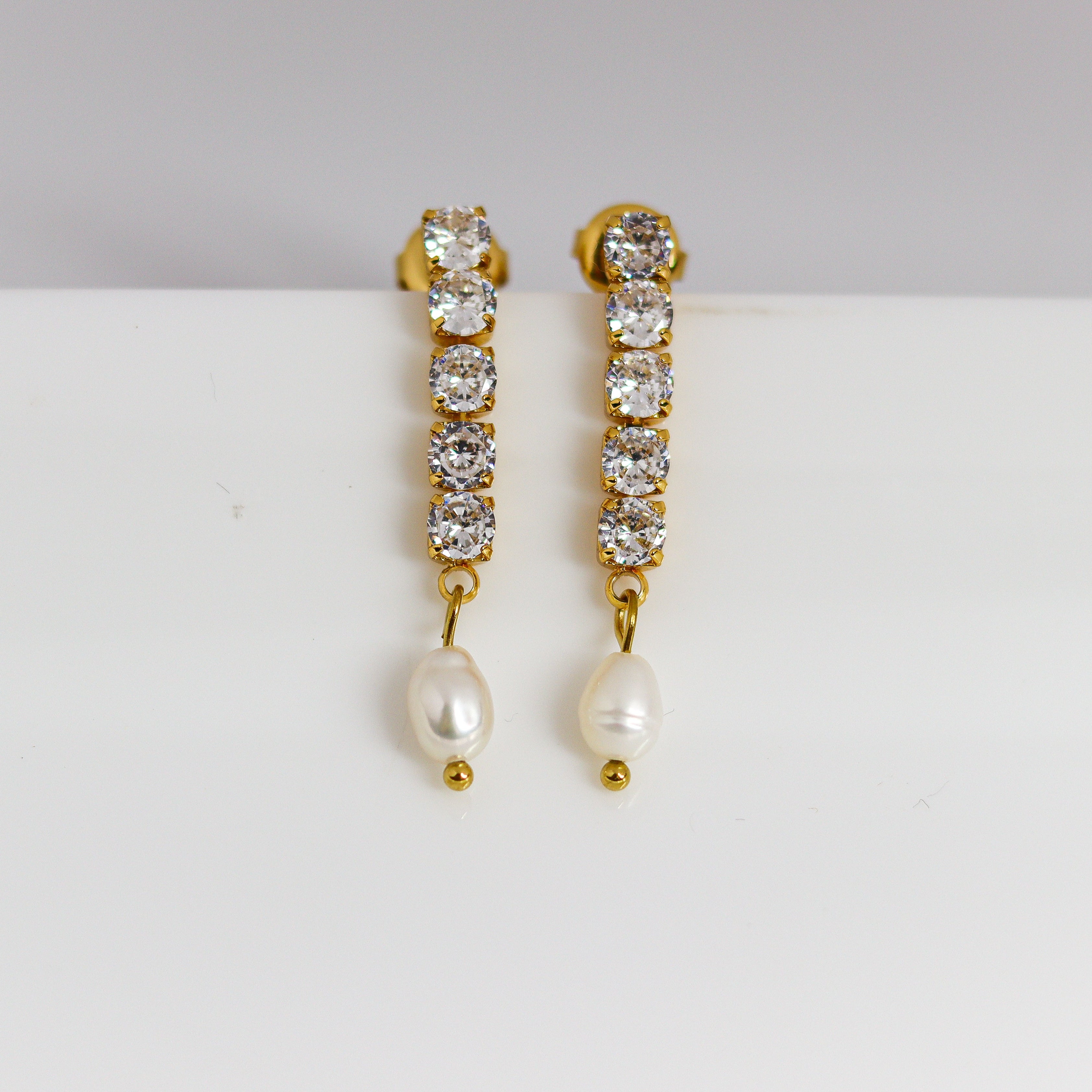 Gold earrings with crystal stones and pearls on a white background