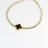 Gold bracelet with a black clover-shaped charm on a white background