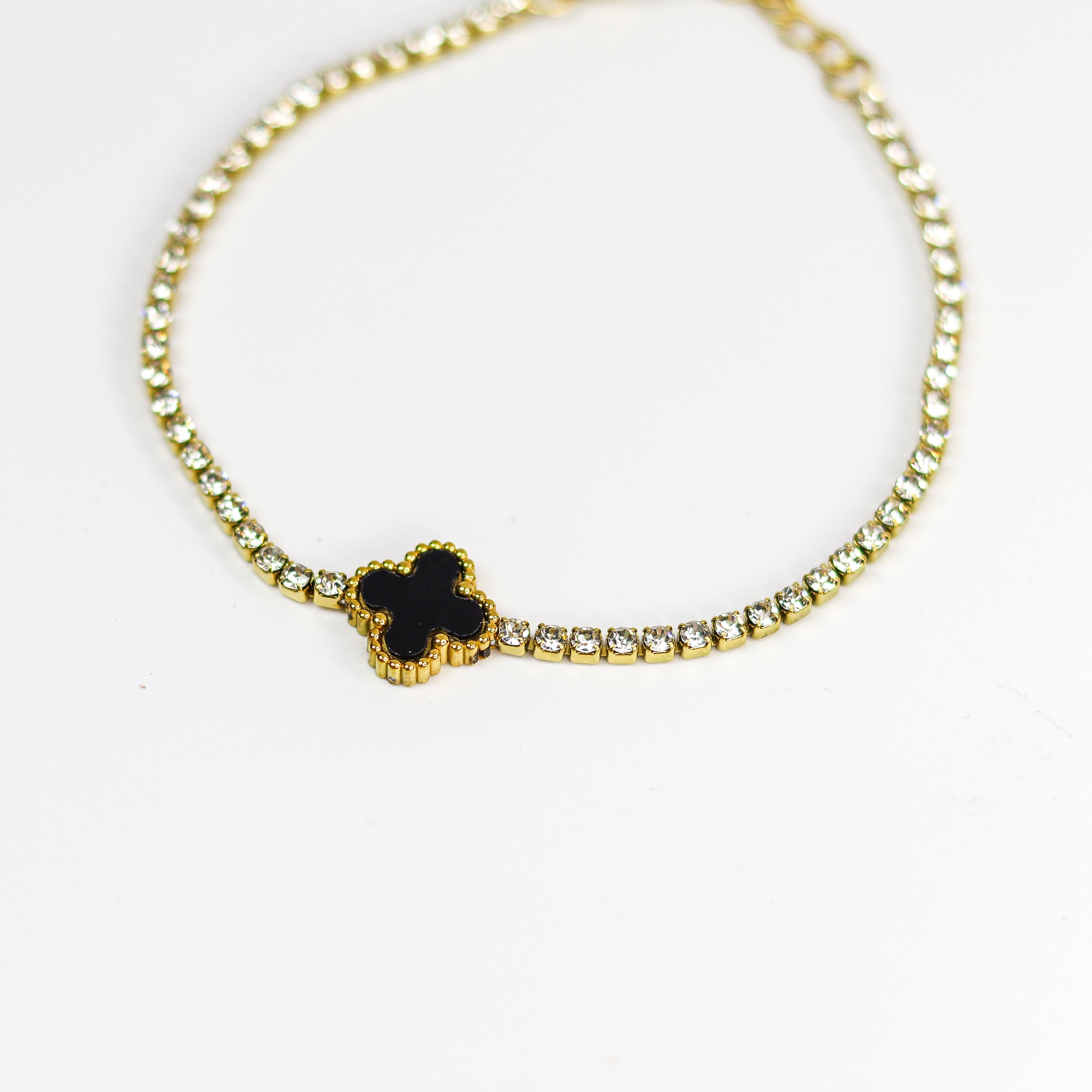 Gold bracelet with a black clover-shaped charm on a white background
