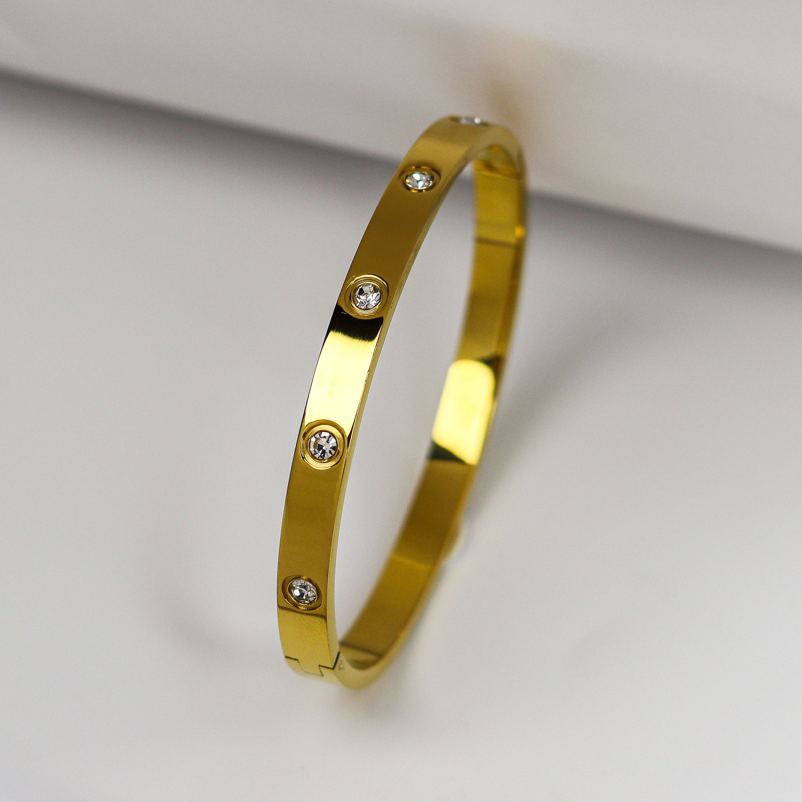 Gold bracelet with small diamonds on a light gray background