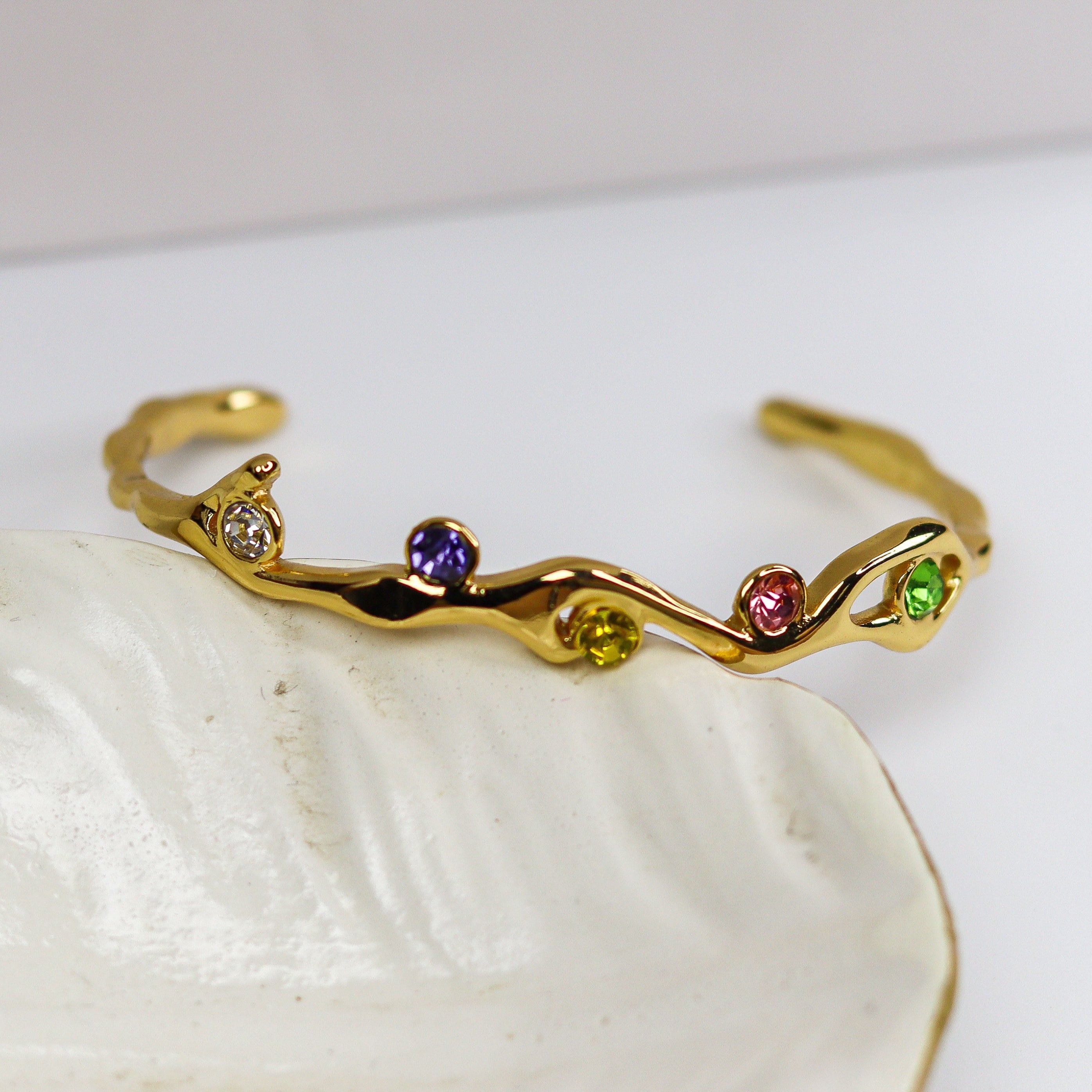 Gold bracelet with colorful stones on a white shell