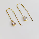 Gold earrings with teardrop-shaped gemstones on a light gray background