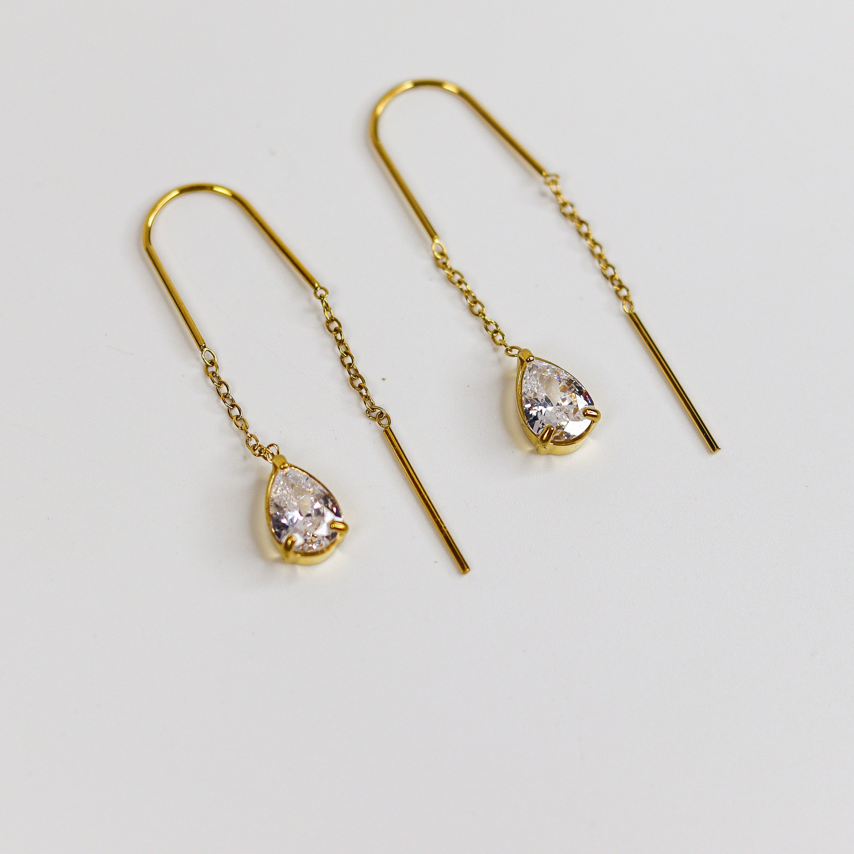 Gold earrings with teardrop-shaped gemstones on a light gray background