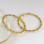 Two gold bracelets on a white dish with a white background