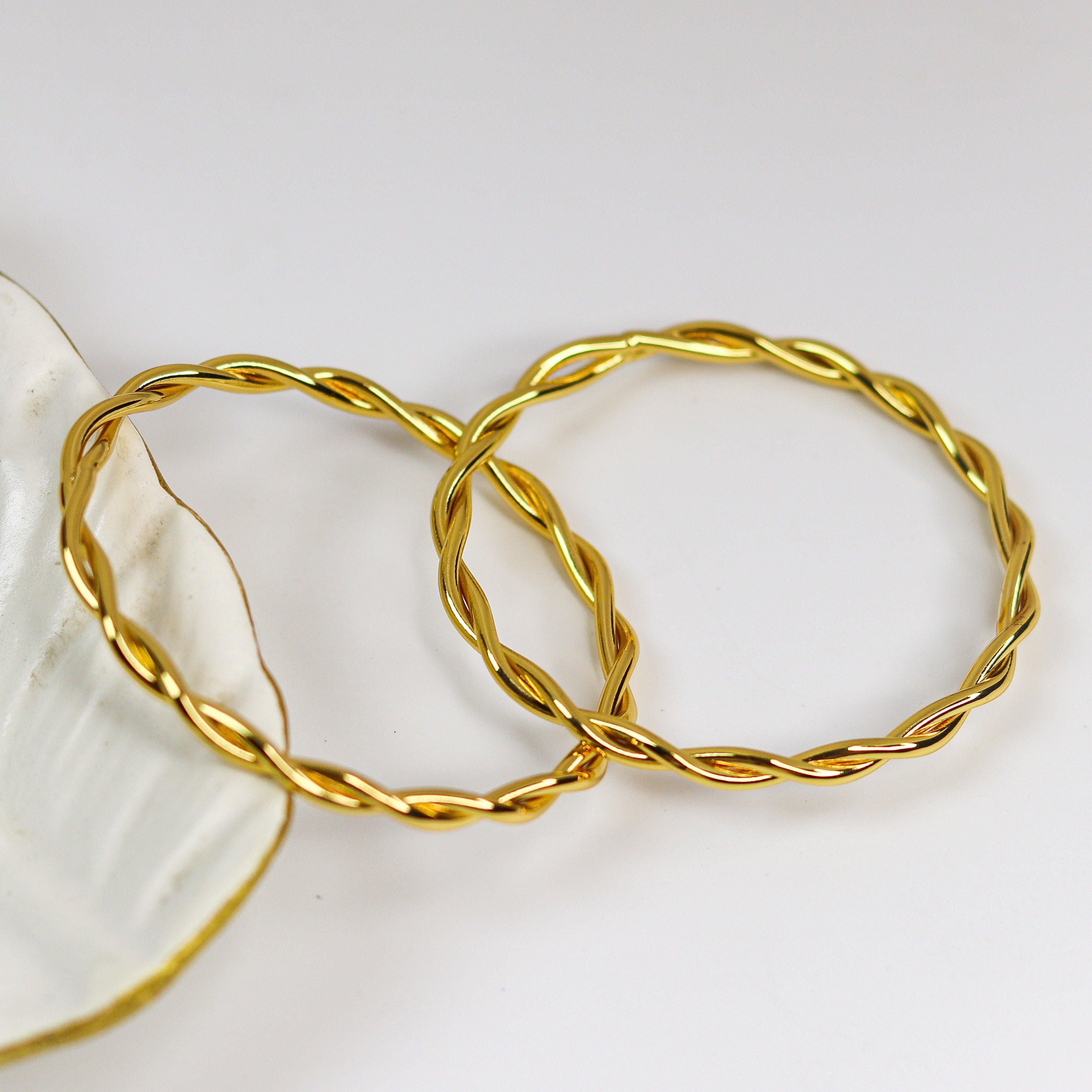 Two gold bracelets on a white dish with a white background