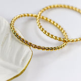 Two gold bracelets on a white dish with a white background