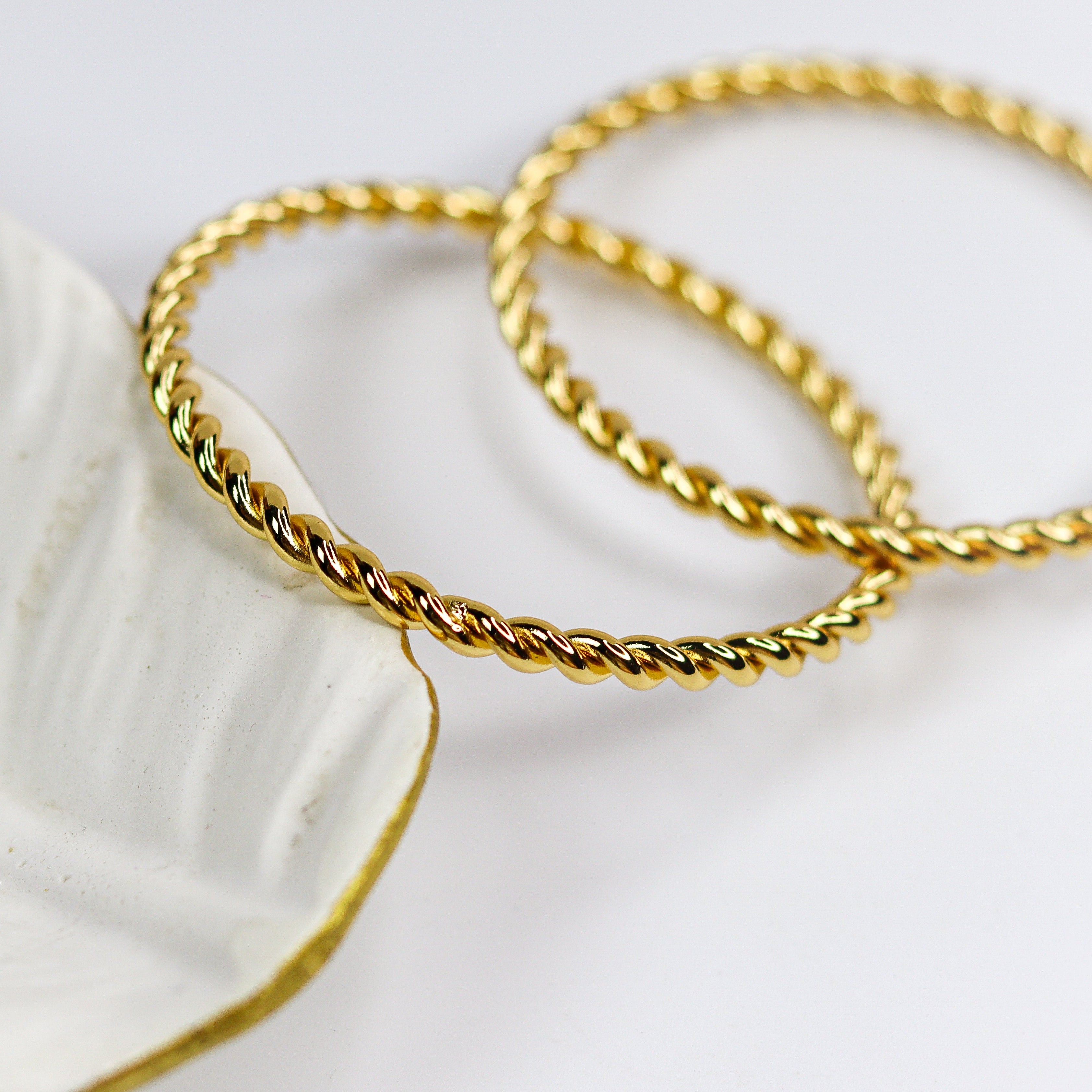 Two gold bracelets on a white dish with a white background