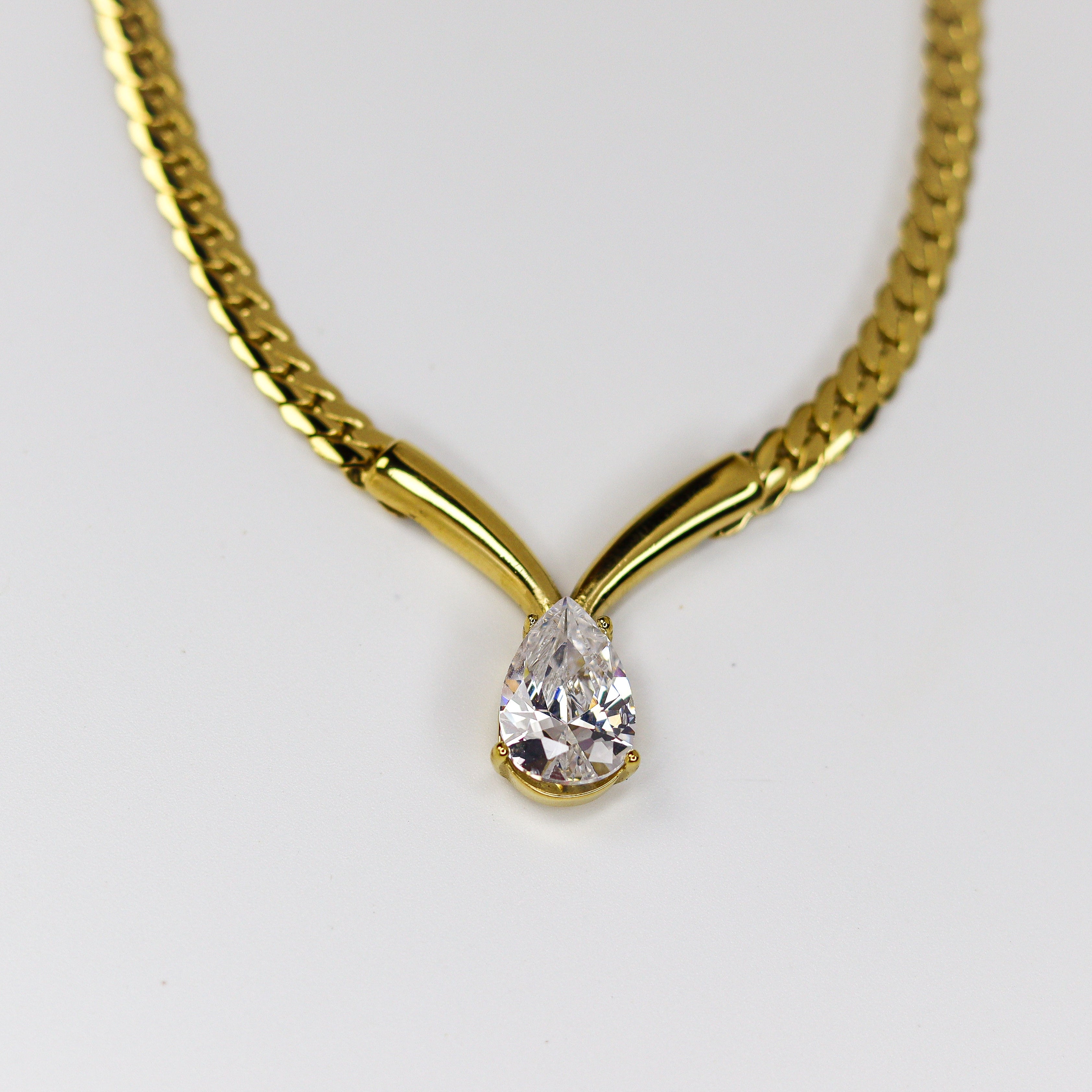 Gold necklace with a teardrop-shaped diamond pendant on a white background