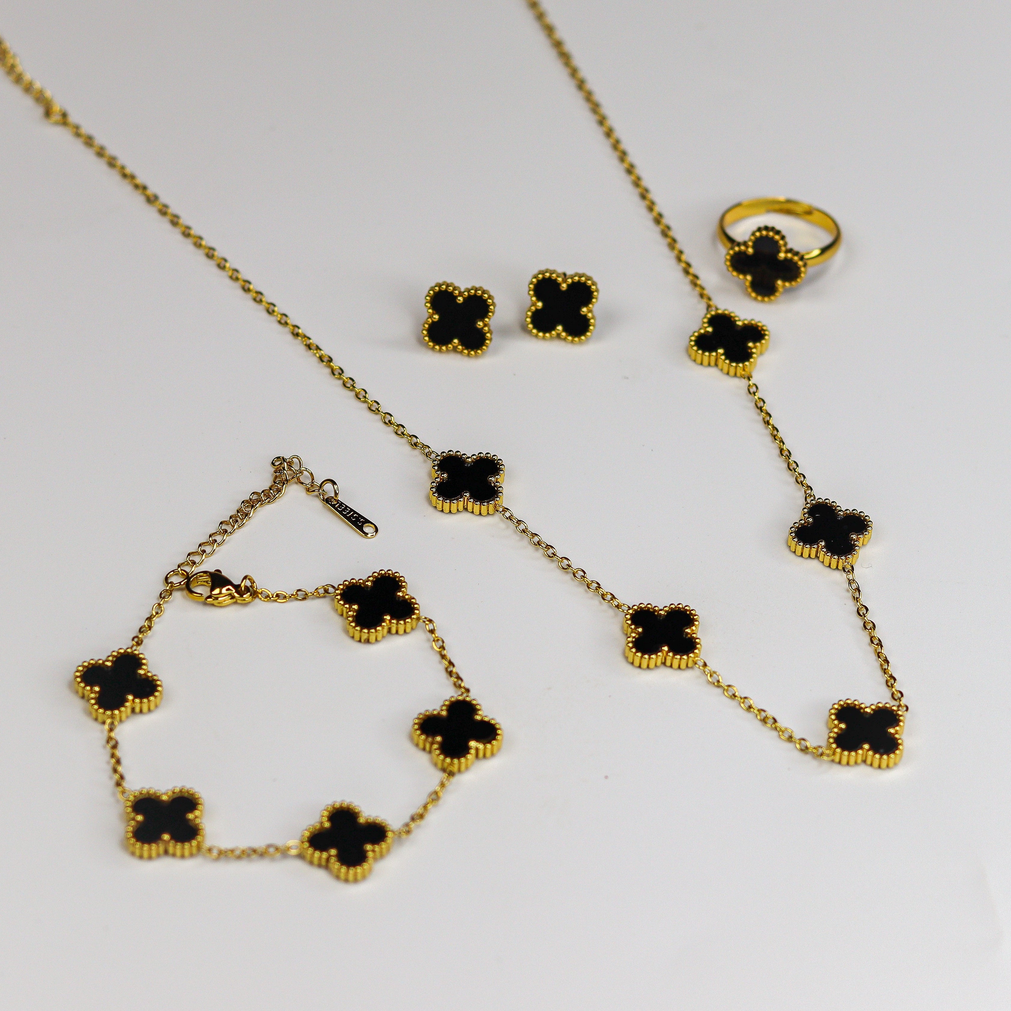 Gold necklace with black clover-shaped charms on a white background