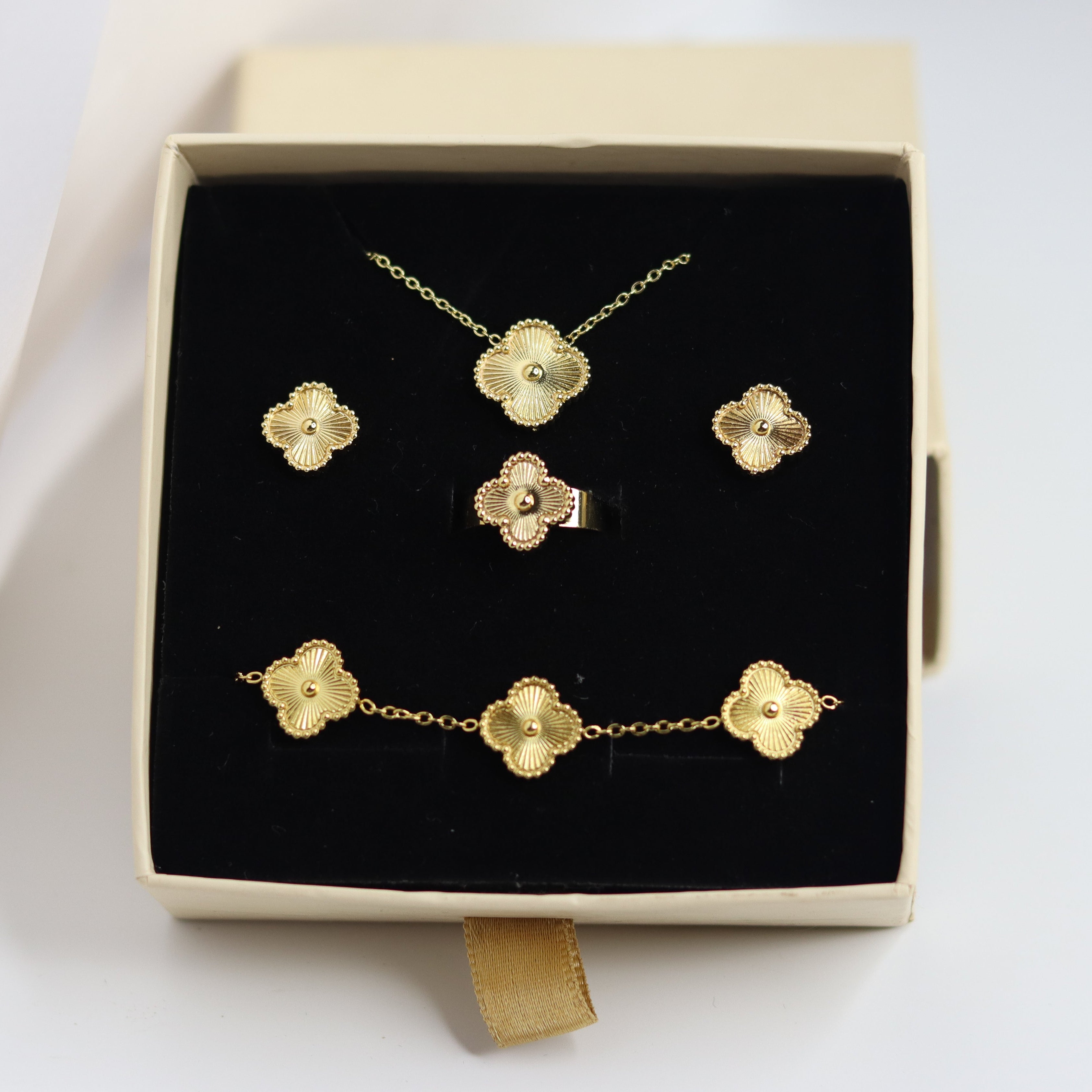 Gold jewelry set including necklace, earrings, and bracelet in a box on a white background