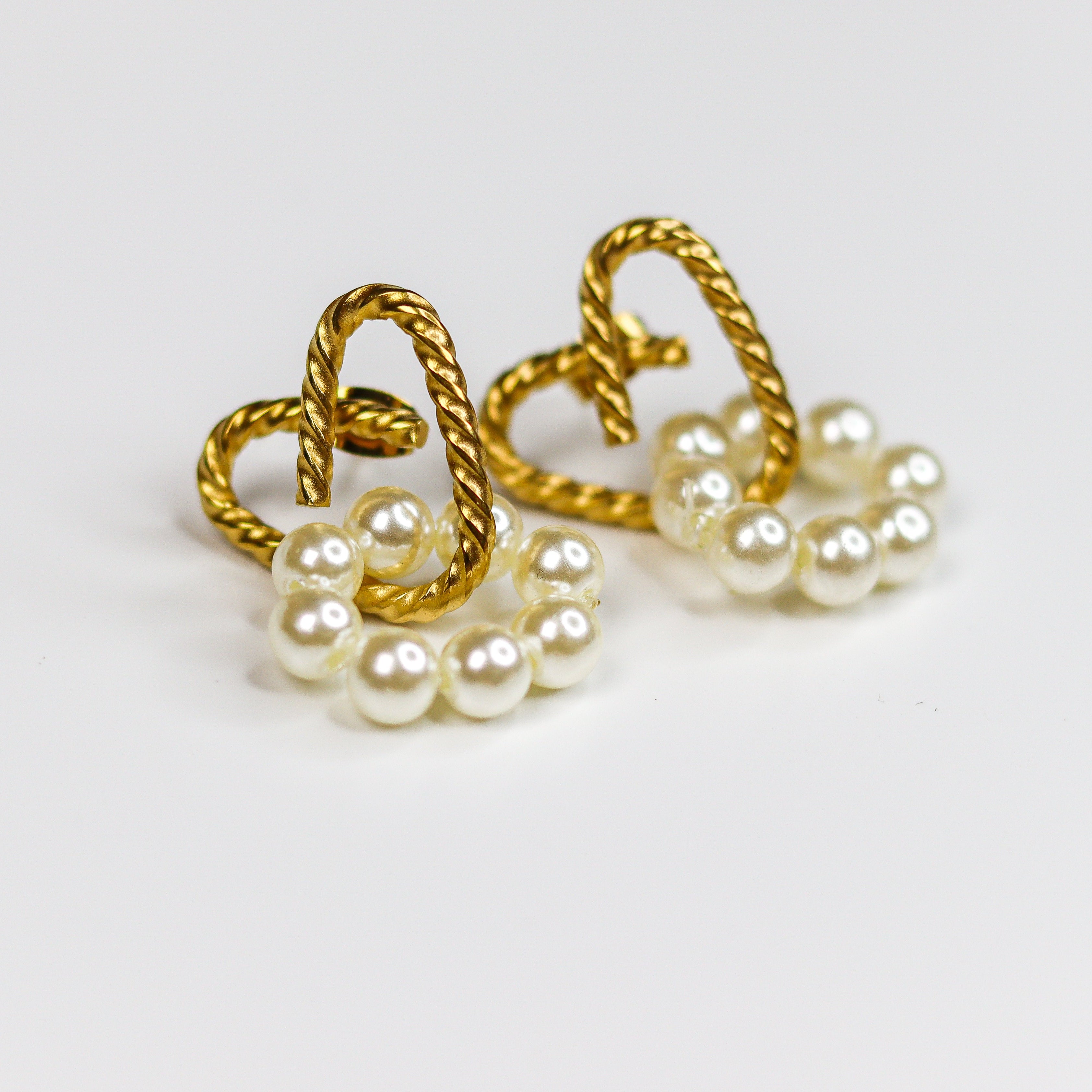 A pair of gold heart-shaped hoop earrings with dangling clusters of white faux pearls, shown on a plain white background.